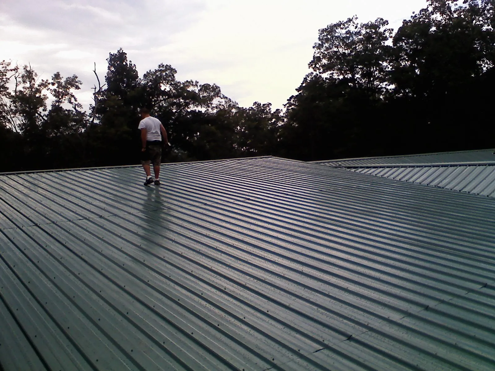 Roofer walking a wide expanse of new green metal roofing in Pulaski